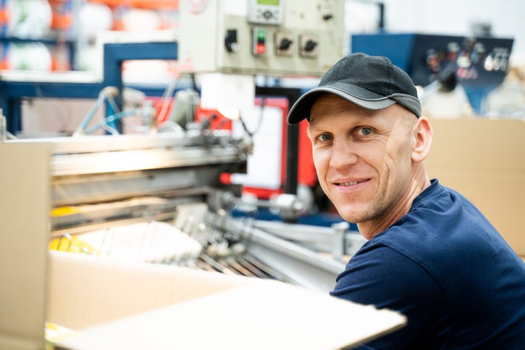 Uśmiechnięty mężczyzna stojący w fabryce obok maszyny.
